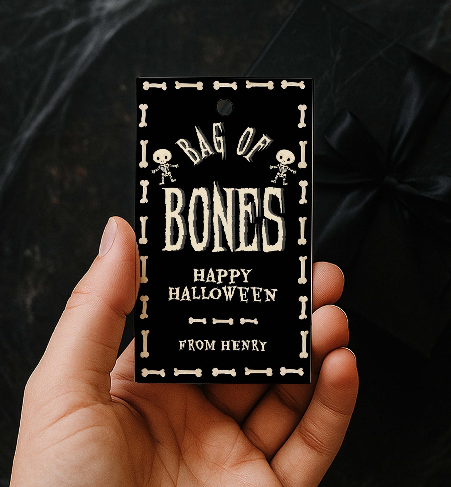Hand holding a 'Bag of Bones' Halloween tag with skeleton designs. Bag Of Bones Treat Tag, Skeleton Bones, Printable Halloween Favor Tags, Trick Or Treat Party Favors, Classroom Halloween Gift