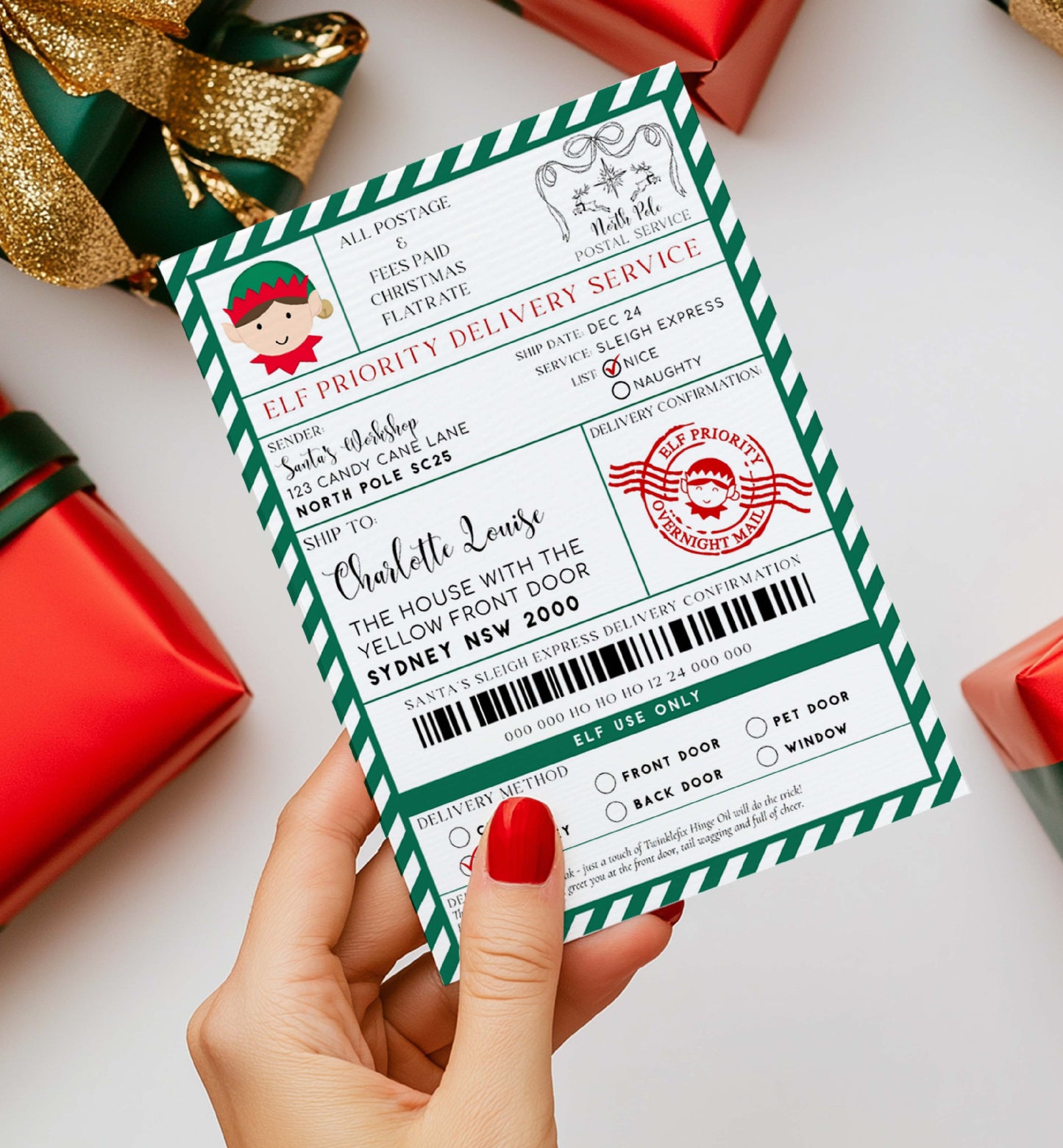 Hand holding a Christmas-themed delivery envelope with red and green design, surrounded by festive decorations. Printable Elf Arrival Box Shipping Label Sticker, North Pole Elf Mail Gift Tag, Santa's Workshop Christmas Special Delivery Shipping Label
