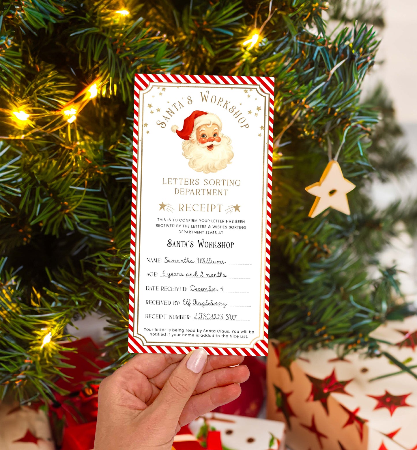 Hand holding a Santa's Workshop letter in front of a Christmas tree with lights and decorations. Printable Letter To Santa Receipt, Santa's Nice List Receipt, Letter From Santa's Workshop, North Pole Mail, Christmas Eve Box Santa Letter