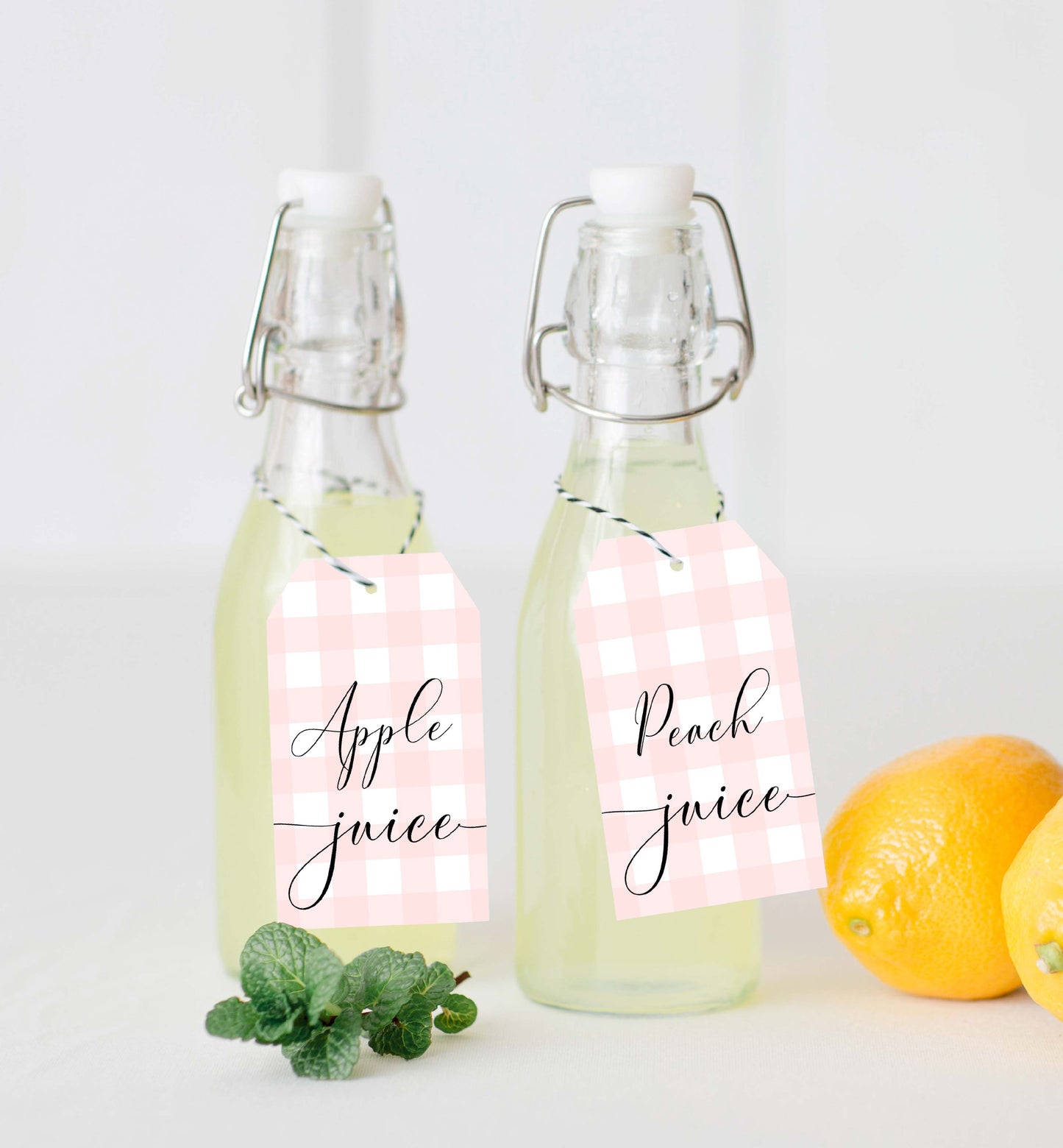 Two glass bottles labeled 'Apple juice' and 'Peach juice' with pink checkered labels on a white background. Printable Mimosa Bar Sign and Juice Tags, Pink Gingham Check, Girl Baby Shower Mom-osa Bar Sign, Baby Shower Mocktails Drinks Sign