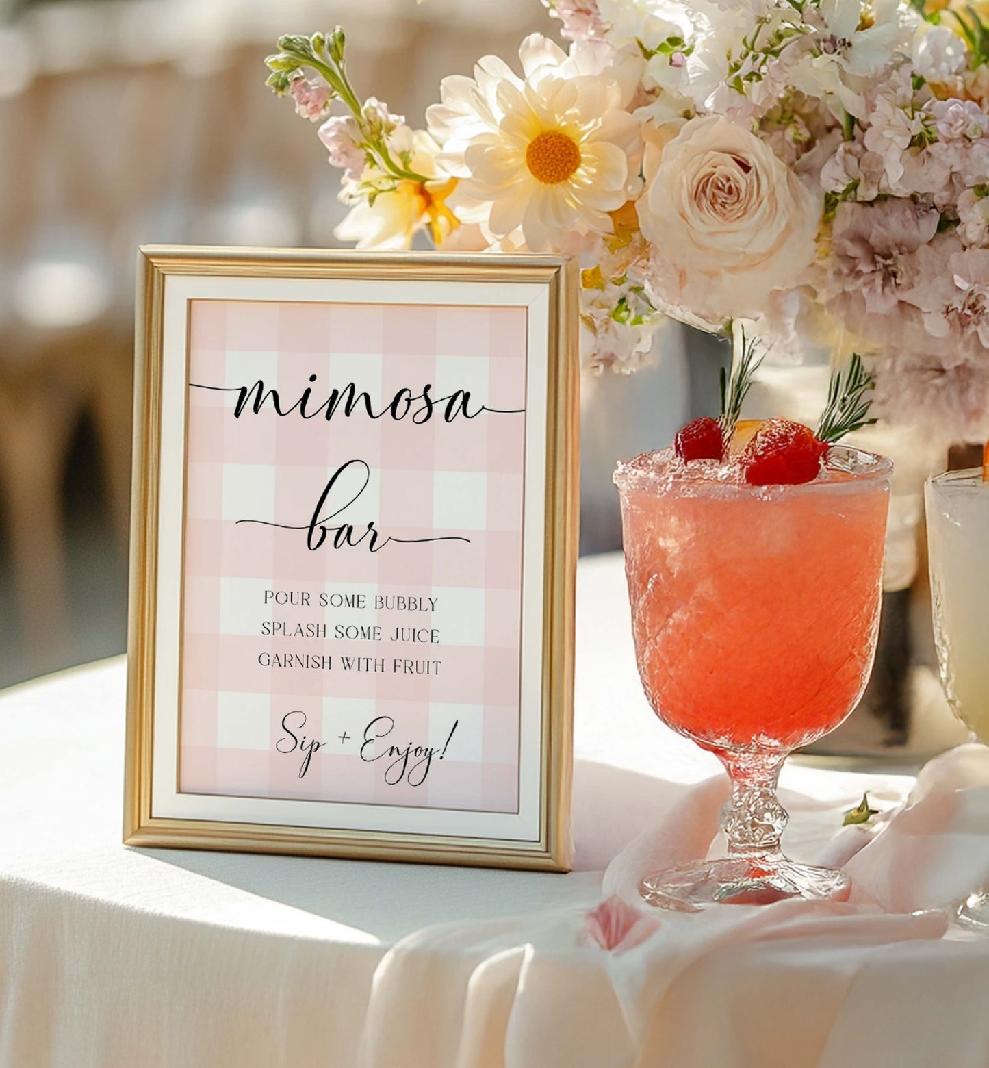 Mimosa bar sign with a glass of pink cocktail and floral arrangement on a table. Printable Mimosa Bar Sign and Juice Tags, Pink Gingham Check, Girl Baby Shower Mom-osa Bar Sign, Baby Shower Mocktails Drinks Sign