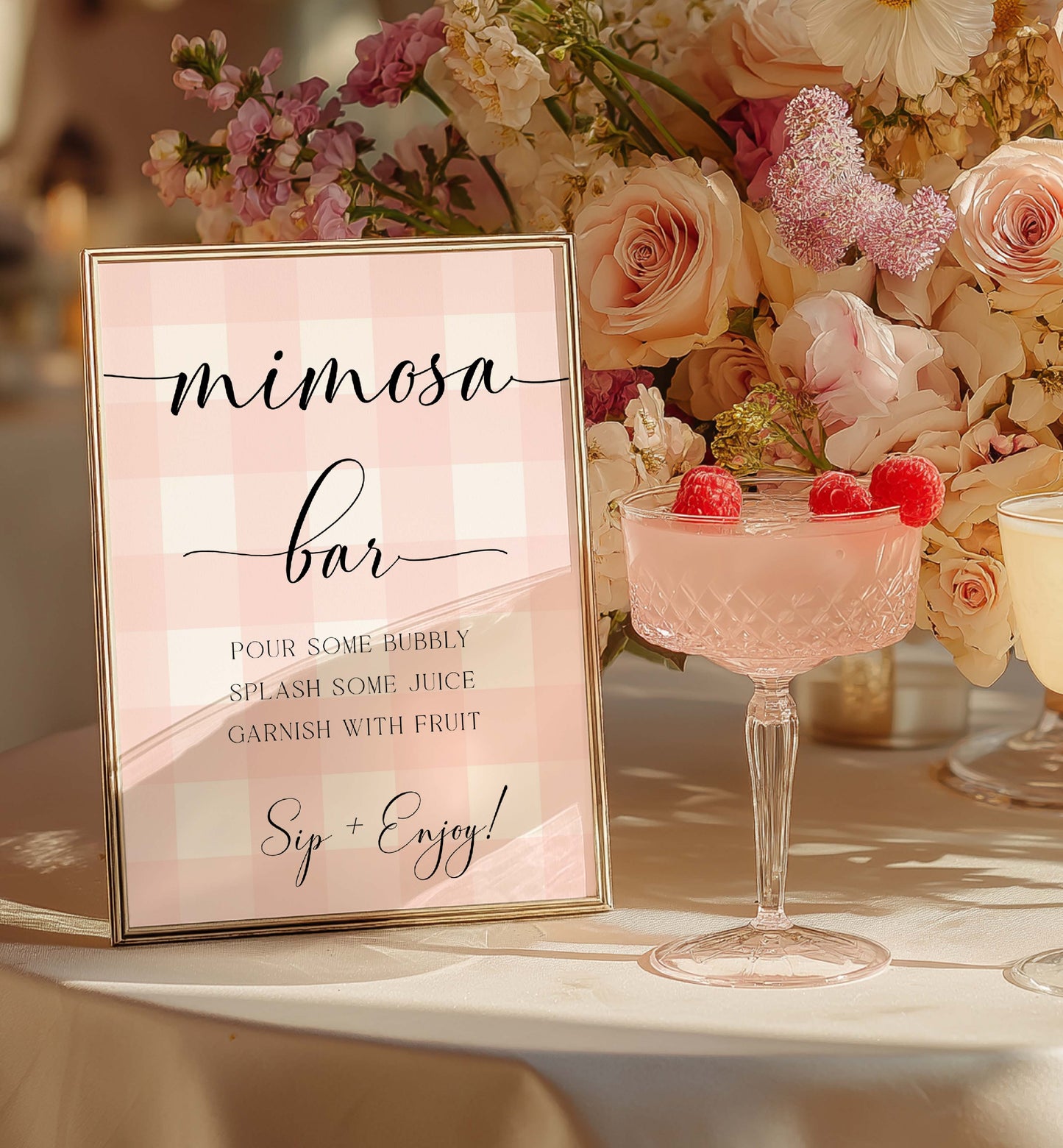 Mimosa bar sign with a glass of pink cocktail garnished with raspberries on a floral decorated table. Printable Mimosa Bar Sign and Juice Tags, Pink Gingham Check, Girl Baby Shower Mom-osa Bar Sign, Baby Shower Mocktails Drinks Sign