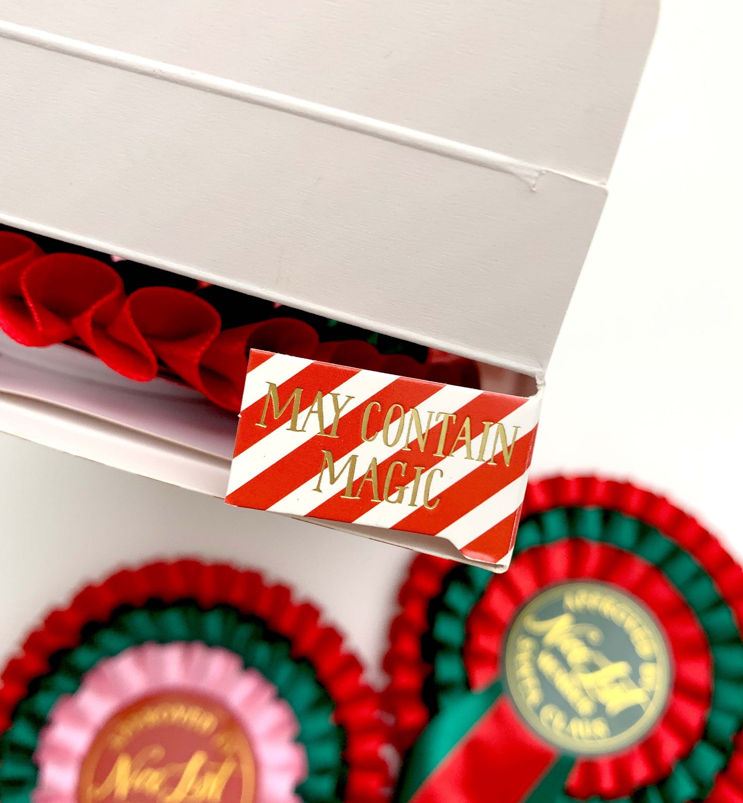 Close-up of a box with a 'May Contain Magic' label, surrounded by decorative ribbons. Nice List Member Rosette Pink Red Green, Christmas Eve Box Gift, Present From Santa Claus, Kids Christmas Gift, Nice List Member Gift