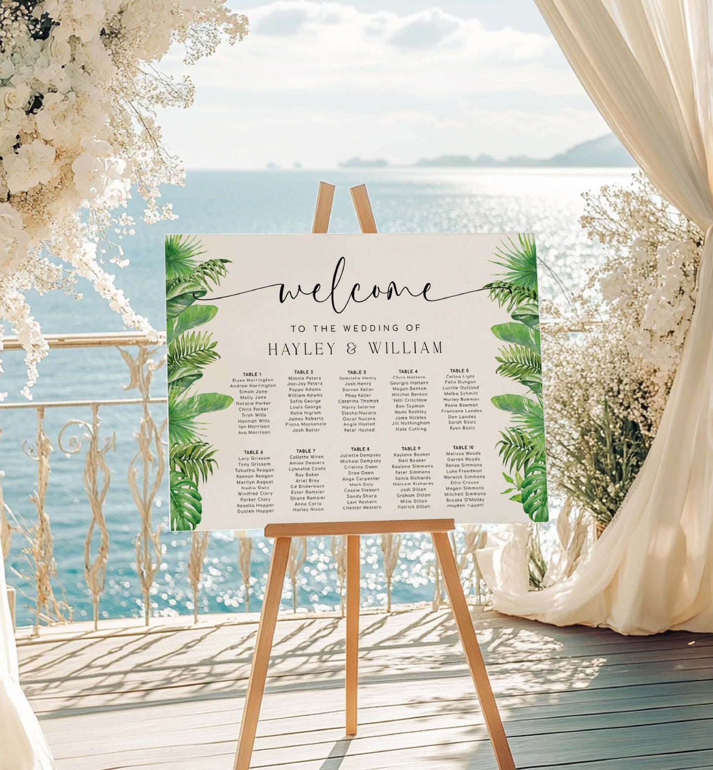 Wedding seating chart on an easel with floral decorations by a waterfront. Tropical Palm Wedding Table Plan, Printable Editable Seating Chart Template, Tropical Greenery Wedding Seating Plan Card, Nantucket Palm