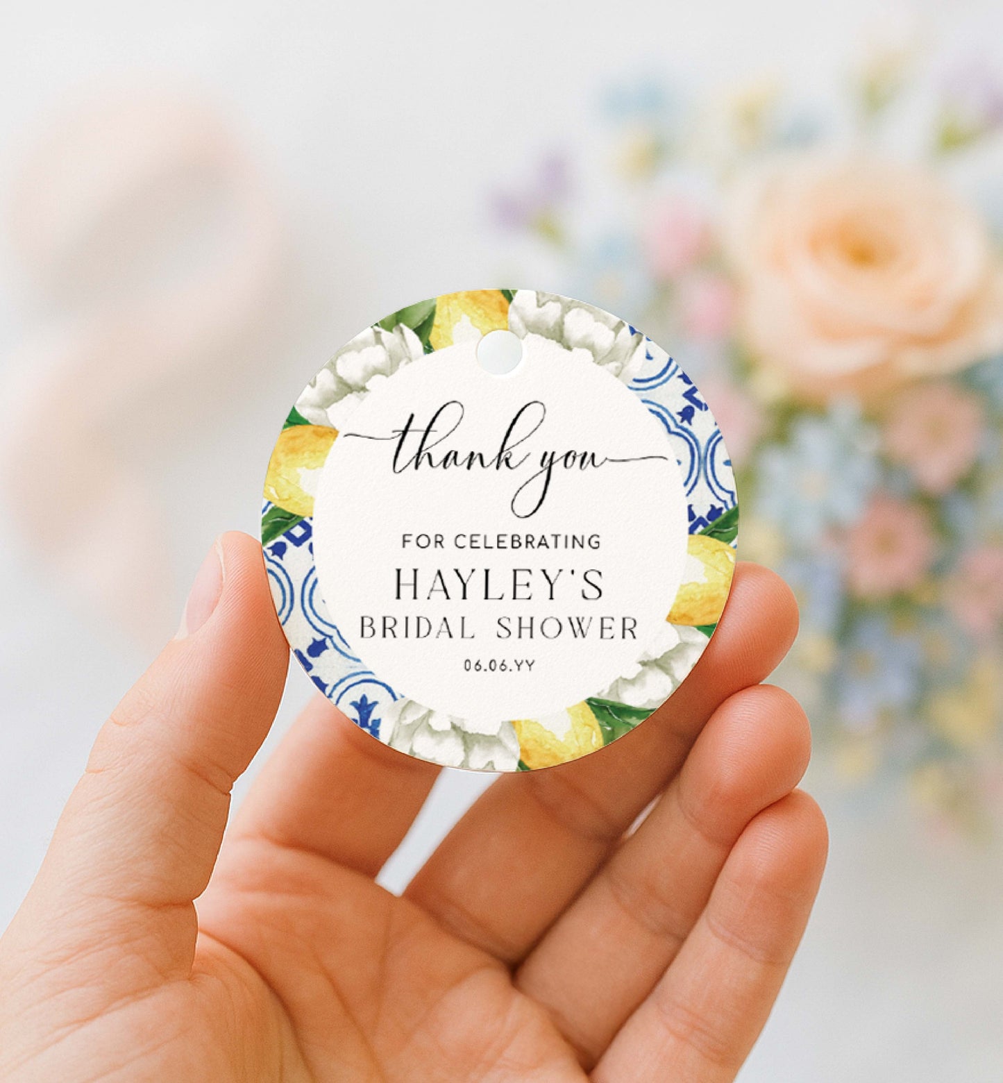 Round favor tag with floral design and text held by a hand, blurred floral background. Printable Thank You Tag, Mediterranean Blue Tile Favor Tags, Lemons Thank You Grazie Tags, Ευχαριστώ Favor Tags, The Med