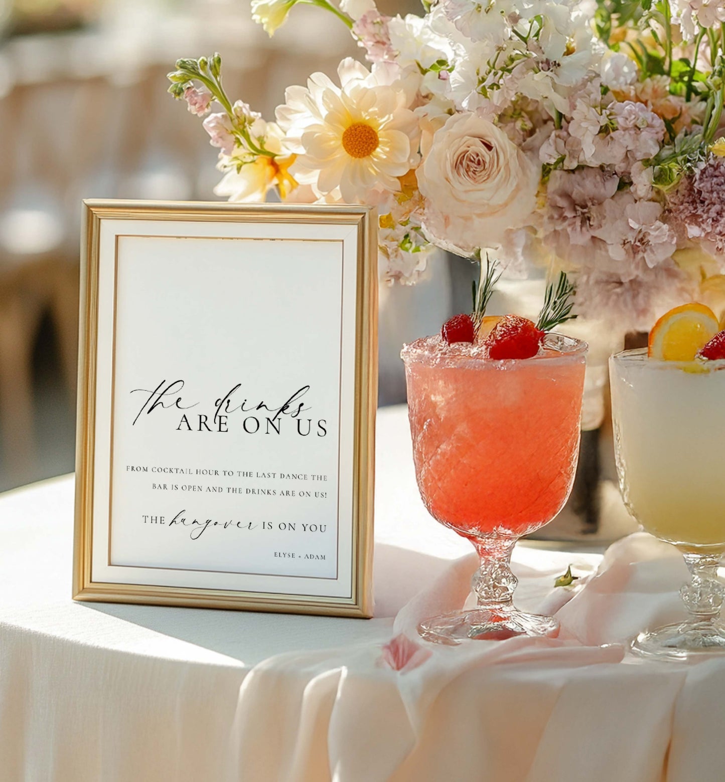 Decorative table setting with cocktails and a sign reading 'The drinks are on us'. Printable Open Bar Sign Template, Minimalist Wedding Open Bar Sign, Printable Drinks Are On Us Sign, Wedding Bar Menu Sign, Ellesmere