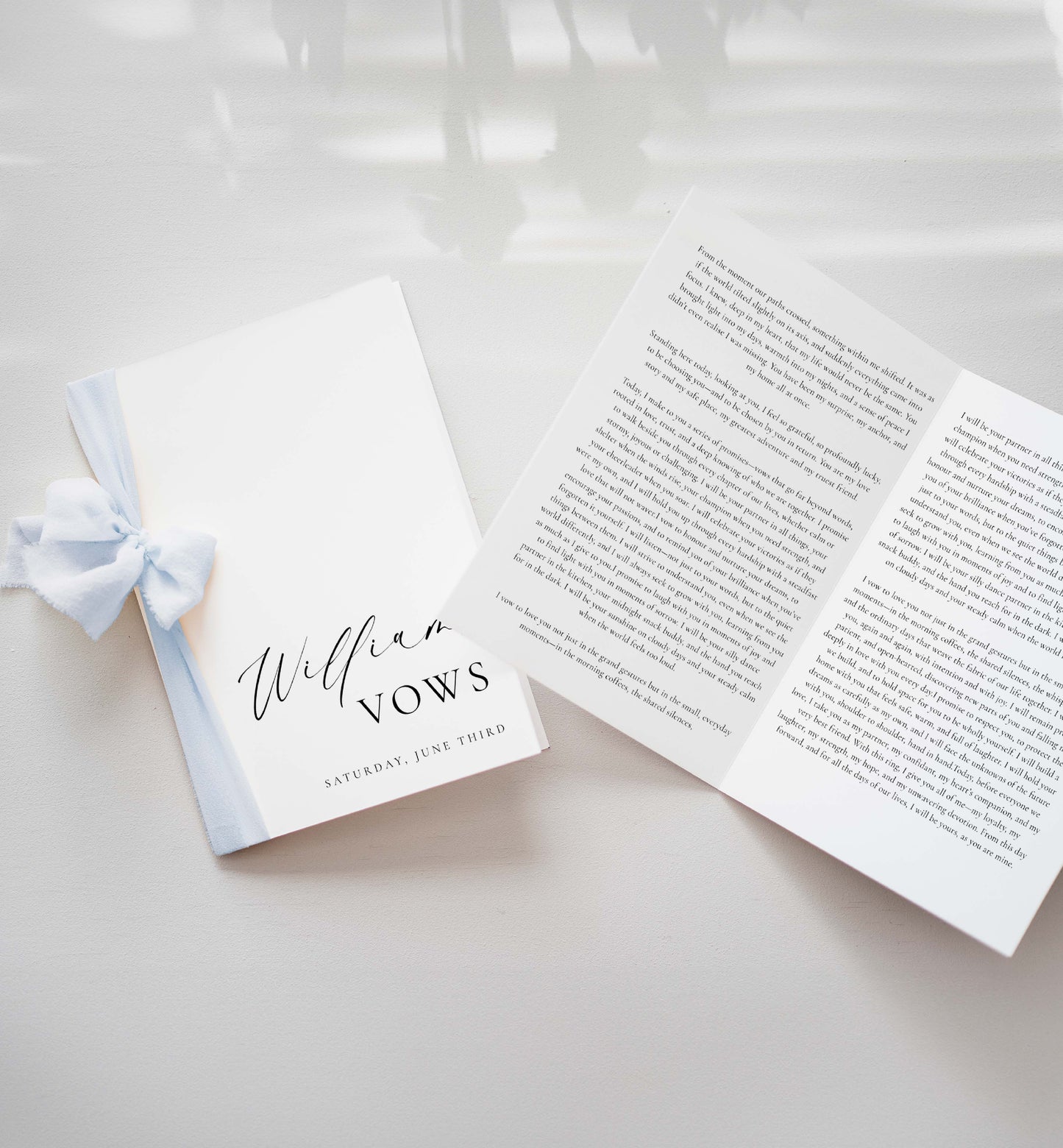 Open book with printed text and a small notebook with a blue ribbon on a light background. Printable His And Her Vow Books, Bride and Groom Wedding Day Card Template, Minimalist Wedding Vows Card, Wedding Ceremony Card Ellesmere