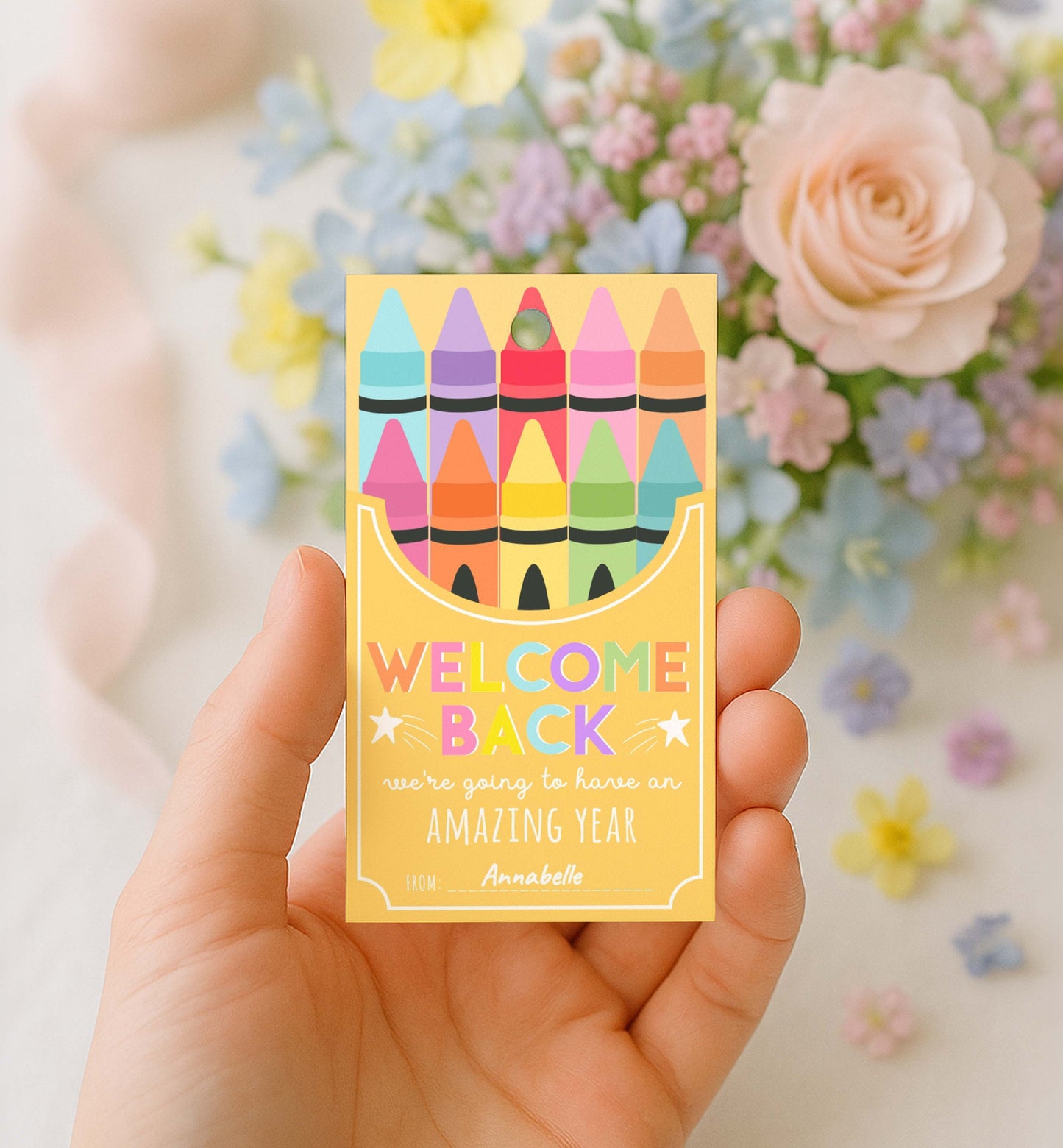 Hand holding a card with colorful crayons and 'Welcome Back' text, flowers in the background. Printable Back To School Tag Template, Welcome Back To School Pencil Holder Tag, New School Year Classroom Gift, Crayon Gift