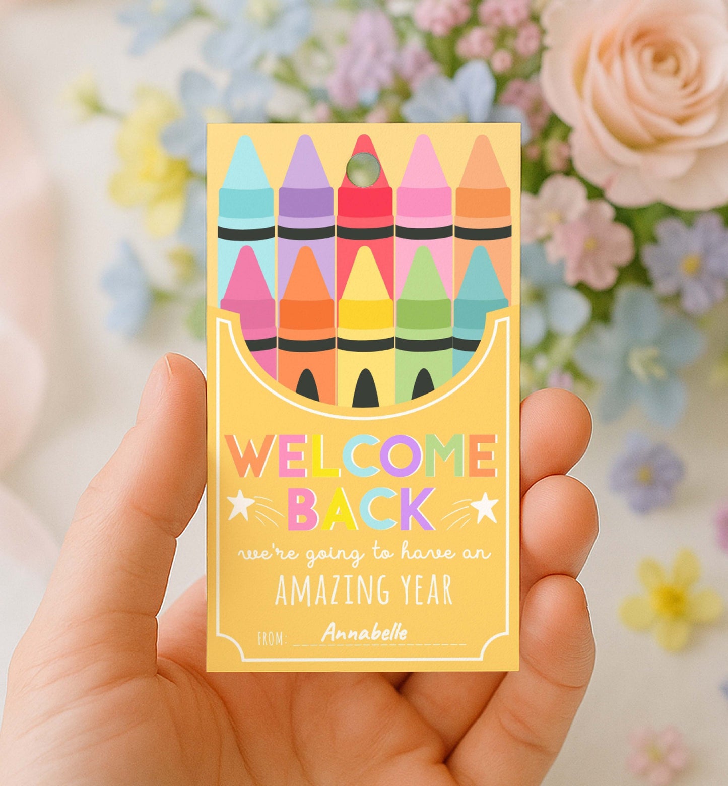 Hand holding a card with colorful crayons and 'Welcome Back' text against a floral background. Printable Back To School Tag Template, Welcome Back To School Pencil Holder Tag, New School Year Classroom Gift, Crayon Gift