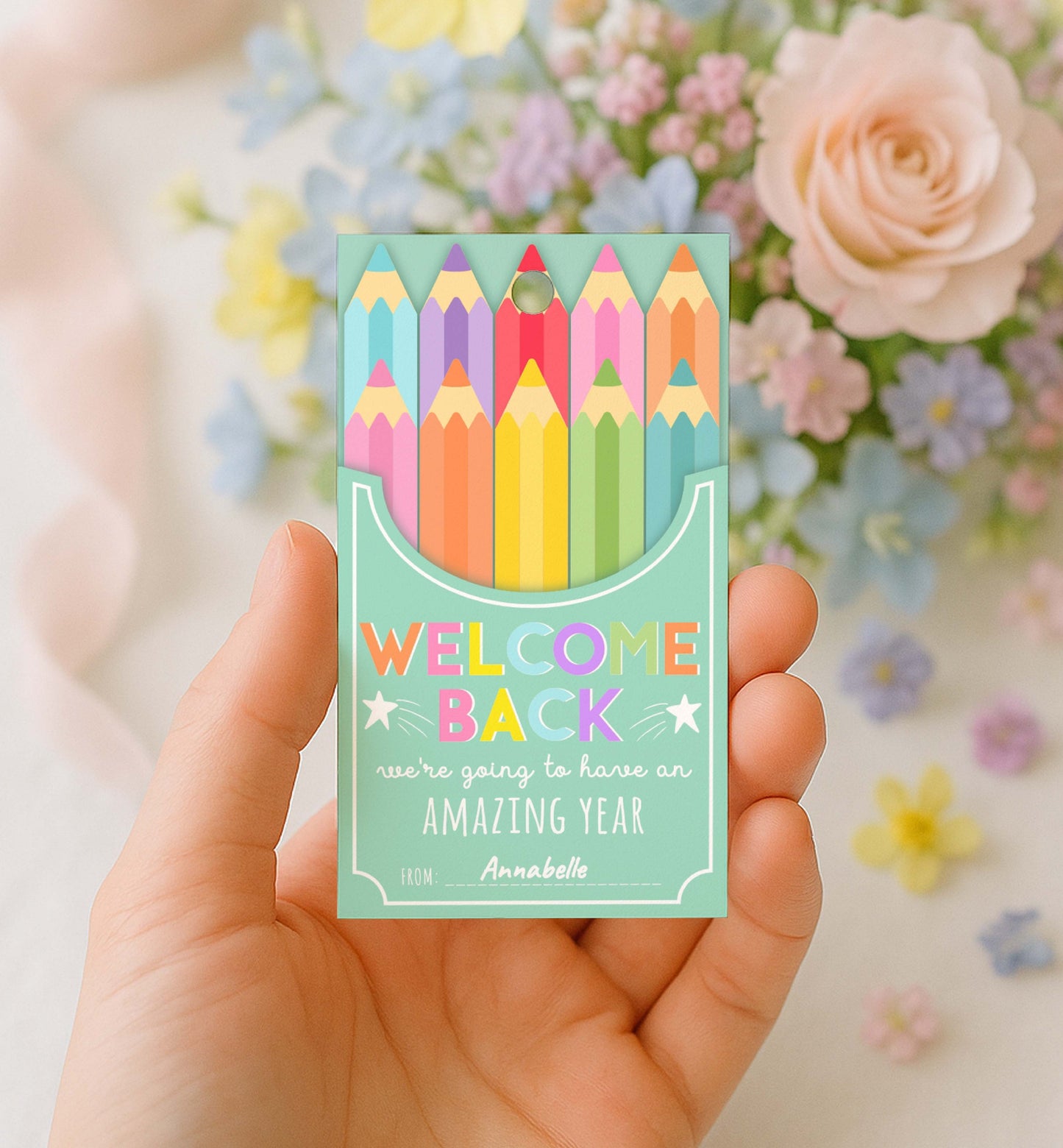 Packaged colorful pencils with 'Welcome Back' text held by a hand against a floral background. Printable Back To School Tag Template, Welcome Back To School Pencil Holder Tag, New School Year Classroom Gift, Crayon Gift