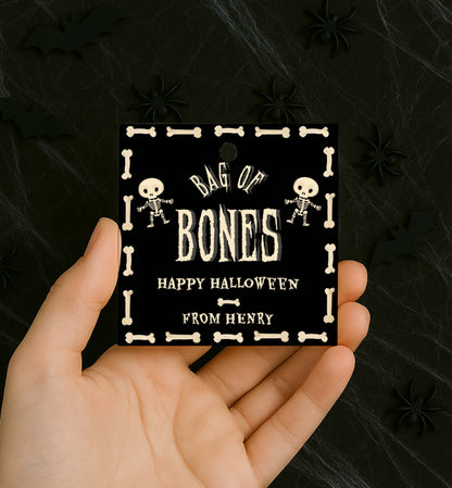 Hand holding a 'Bag of Bones' Halloween tag with skeleton designs on a dark background. Bag Of Bones Treat Tag, Skeleton Bones, Printable Halloween Favor Tags, Trick Or Treat Party Favors, Classroom Halloween Gift