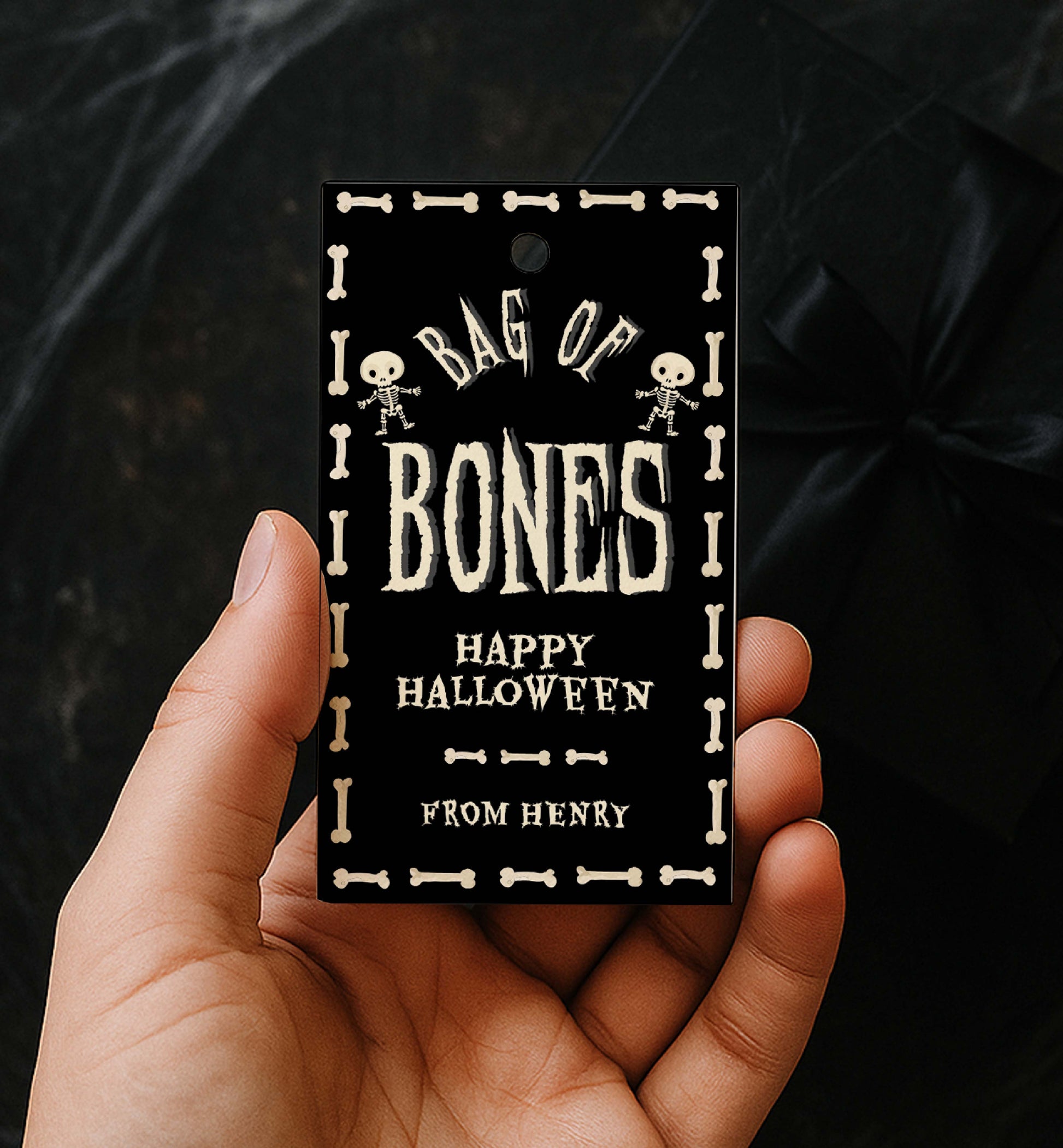 Hand holding a 'Bag of Bones' Halloween tag with skeleton designs. Bag Of Bones Treat Tag, Skeleton Bones, Printable Halloween Favor Tags, Trick Or Treat Party Favors, Classroom Halloween Gift