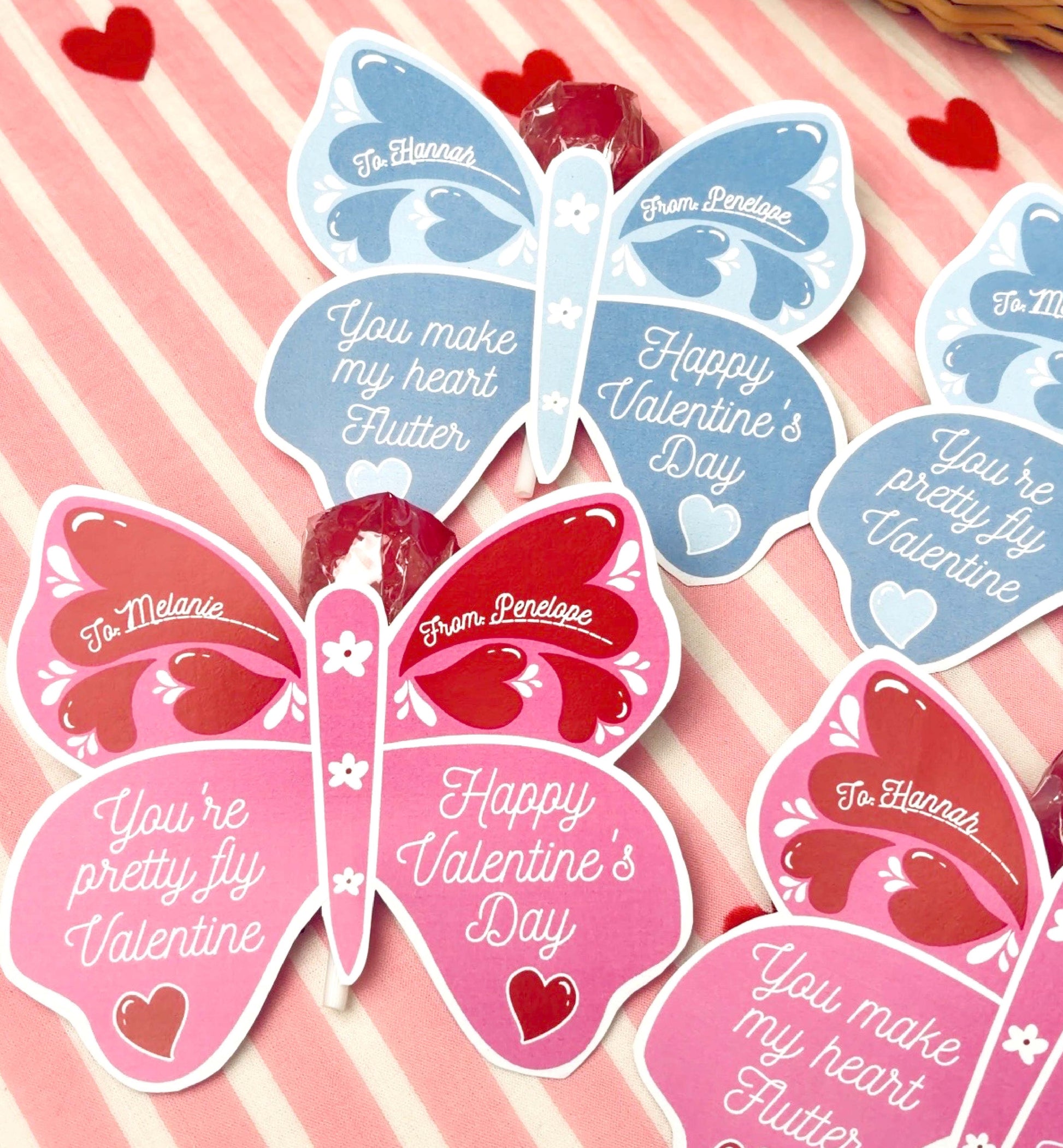 Butterfly-shaped Valentine's Day cards on a pink and white striped background with hearts. Butterfly Valentine's Day Lollipop Tags Template, Printable You Make My Heart Flutter Lollipop Tag, Pretty Fly Sucker Tag, Kids Valentines