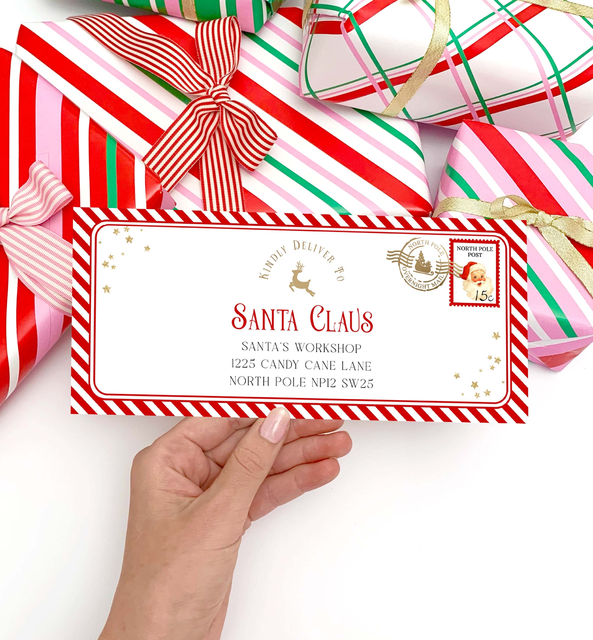 Hand holding a letter addressed to Santa Claus with Christmas presents in the background. Printable Letter To Santa Envelope, Santa North Pole Mail Envelope Template, Christmas Eve Box Santa Letter, Red Stripe