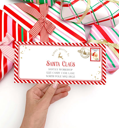 Hand holding a letter addressed to Santa Claus with Christmas presents in the background. Printable Letter To Santa Envelope, Santa North Pole Mail Envelope Template, Christmas Eve Box Santa Letter, Red Stripe
