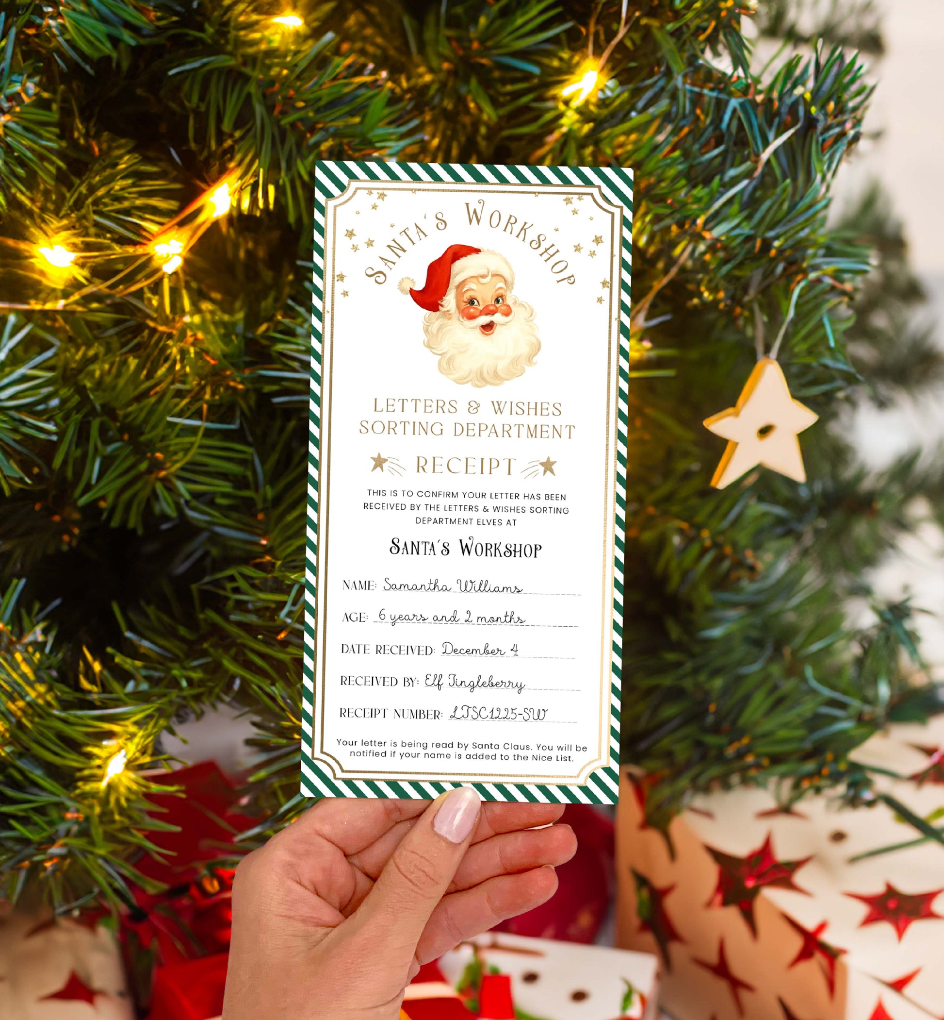 Hand holding a Santa Claus receipt card in front of a decorated Christmas tree with lights and presents. Printable Letter To Santa Receipt, Santa's Nice List Receipt, Letter From Santa's Workshop, North Pole Mail, Christmas Eve Box Santa Letter
