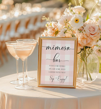 Mimosa bar setup with glasses of pink champagne and a sign on a table. Printable Mimosa Bar Sign and Juice Tags, Pink Gingham Check, Girl Baby Shower Mom-osa Bar Sign, Baby Shower Mocktails Drinks Sign