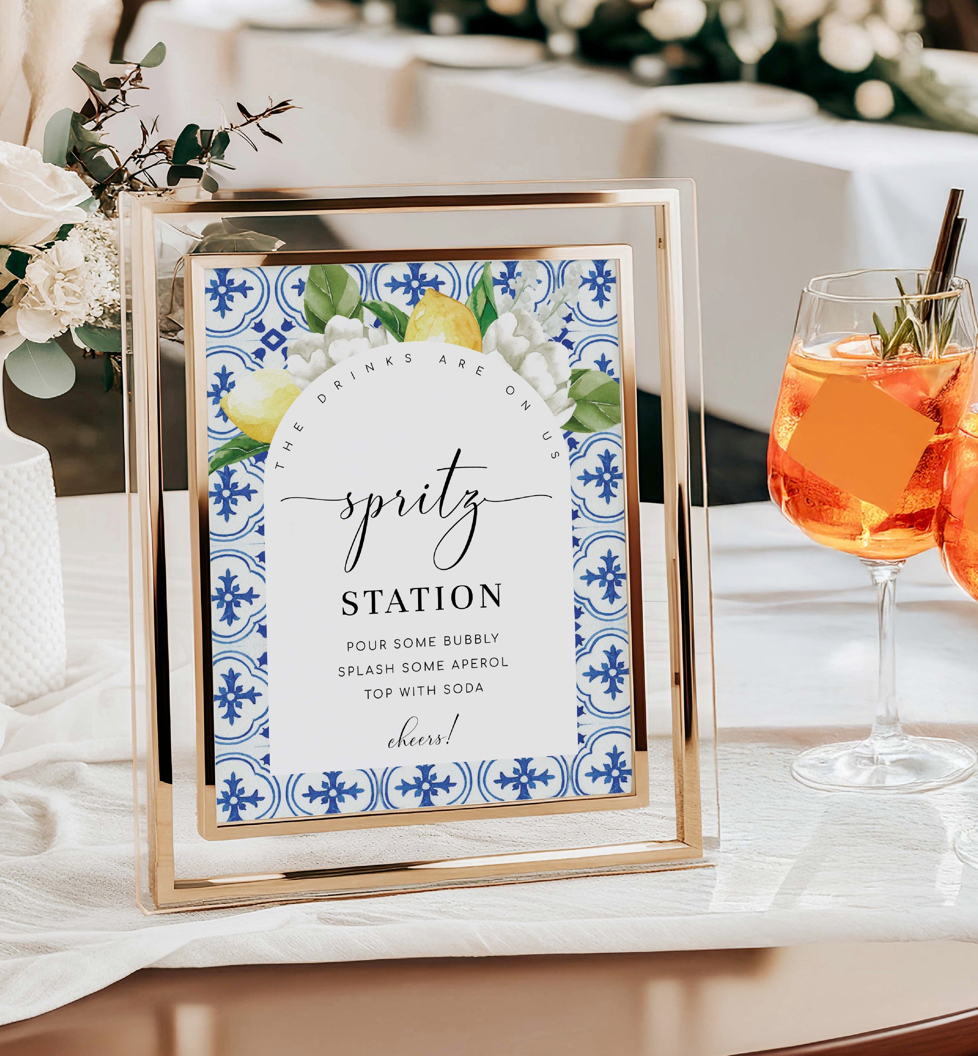 Framed sign for a spritz station on a table with drinks and flowers Printable Spritz Station Sign, Orange Spritz Cocktail Sign, Mediterranean Blue Tile, Lemons Wedding Cocktail Bar Sign, Signature Drinks Sign