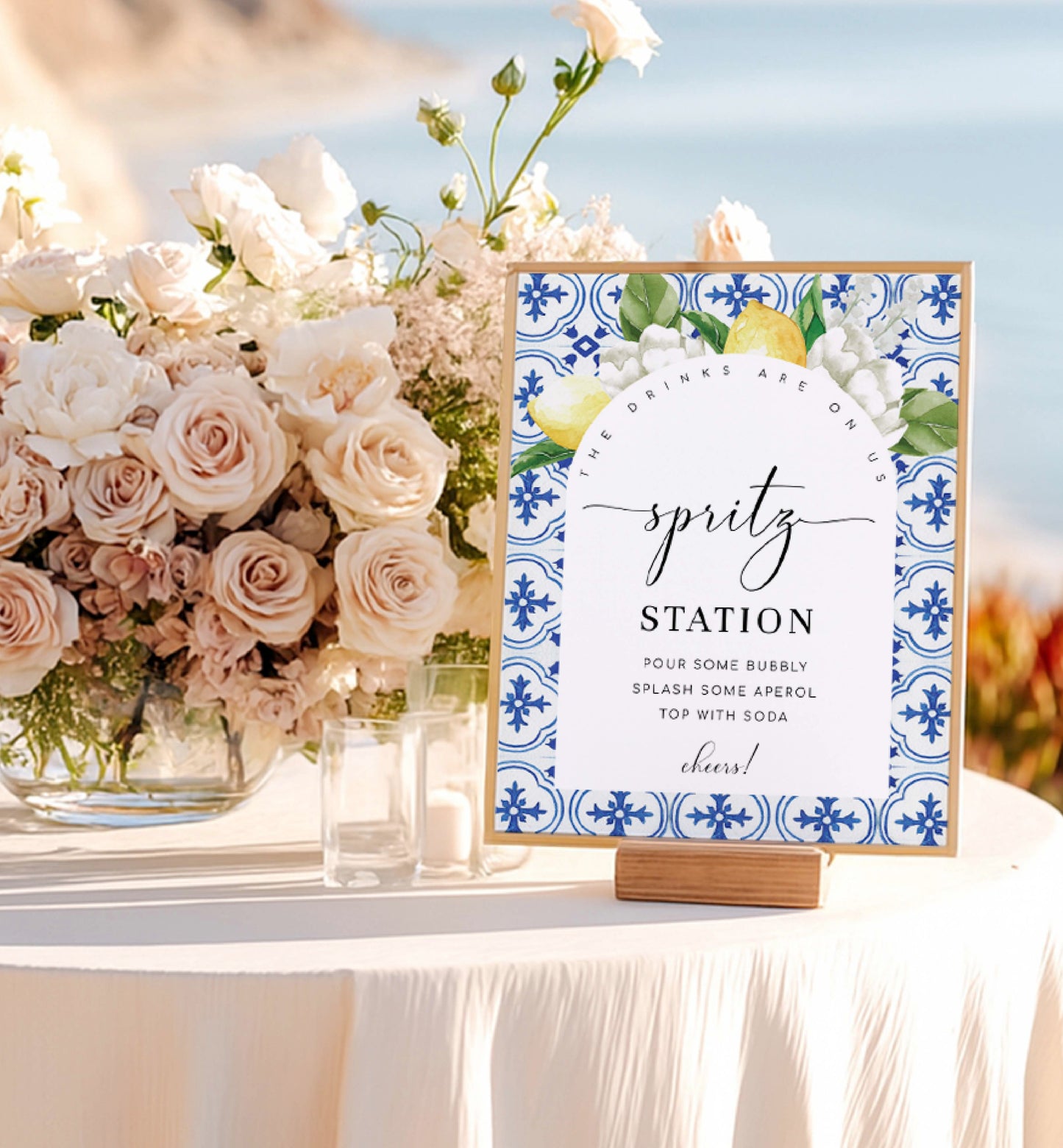 Decorative sign for a 'spritz station' with floral arrangement on a table outdoors. Printable Spritz Station Sign, Orange Spritz Cocktail Sign, Mediterranean Blue Tile, Lemons Wedding Cocktail Bar Sign, Signature Drinks Sign