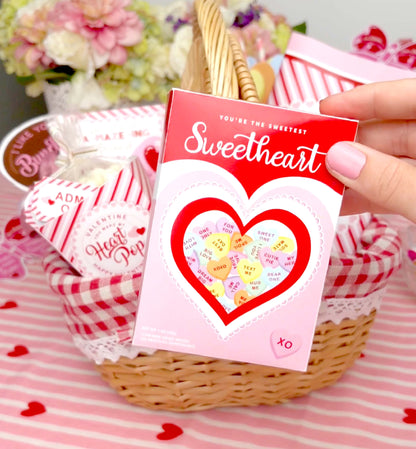 Valentine's Day card with heart design held over a gift basket filled with candy and flowers. Sweetheart Candy Valentine's Day Favor Box (DIY Printable Download)