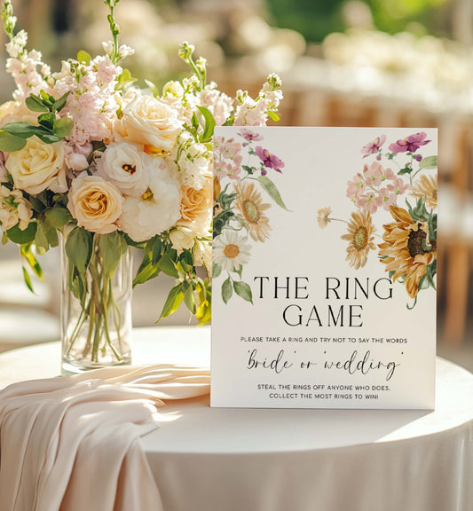 Decorative sign for 'The Ring Game' with floral design on a table with flowers. The Ring Game Sign, Printable Don't Say Bride or Wedding Game Sign, Autumn Fall Sunflower Bridal Shower Game Sign, Mews