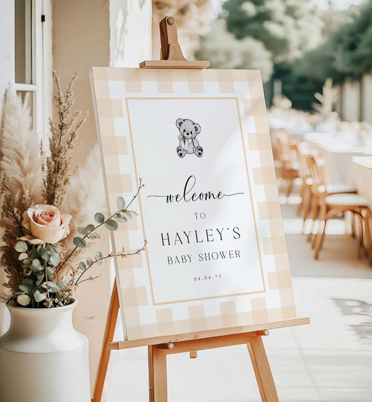 Baby shower welcome sign on an easel with floral decorations and outdoor setting.