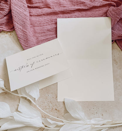 Invitation card with envelope on a textured surface with pink fabric and white flowers. Will You Be Our Mistress of Ceremonies Card, Wedding MC Proposal Card, Minimalist Wedding Card, Wedding Proposal Card, Off White, Ellesmere